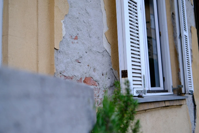 Old building wall with peeling paint and open window shutters.